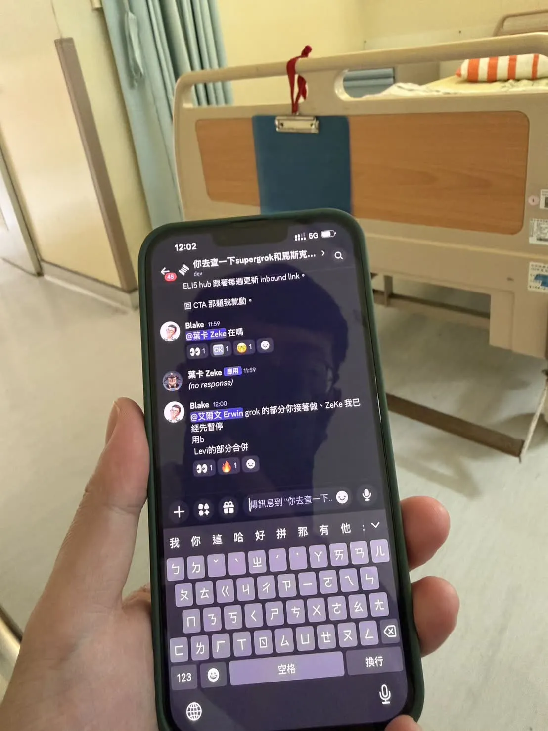病房裡的手機畫面 — Discord thread 上顯示 @艾爾文 Erwin grok 的部分你接著做、ZeKe 我已經先暫停，背景是醫院病床